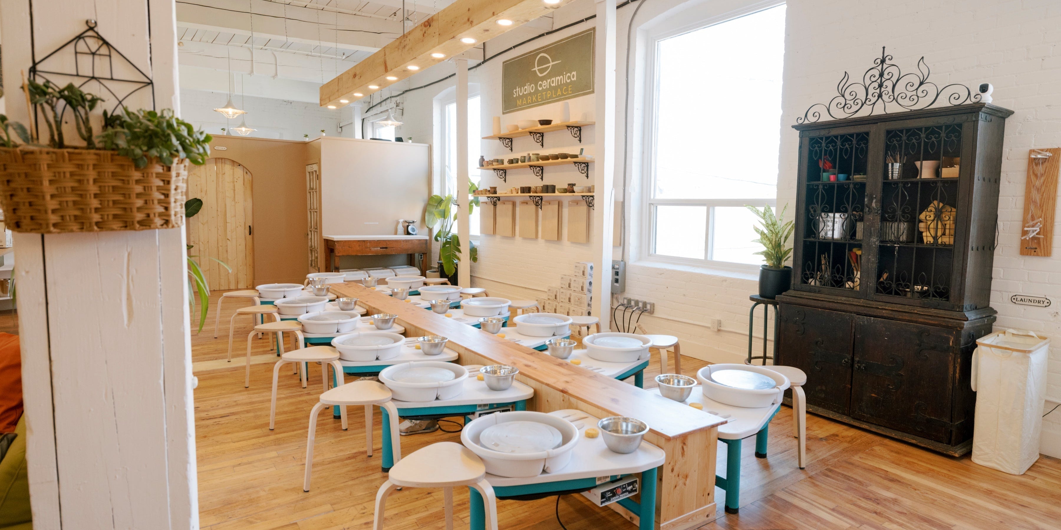 A pinterest worthy pottery studio with lots of wood, a center island flanked by pottery wheels and a wooden light beam. 