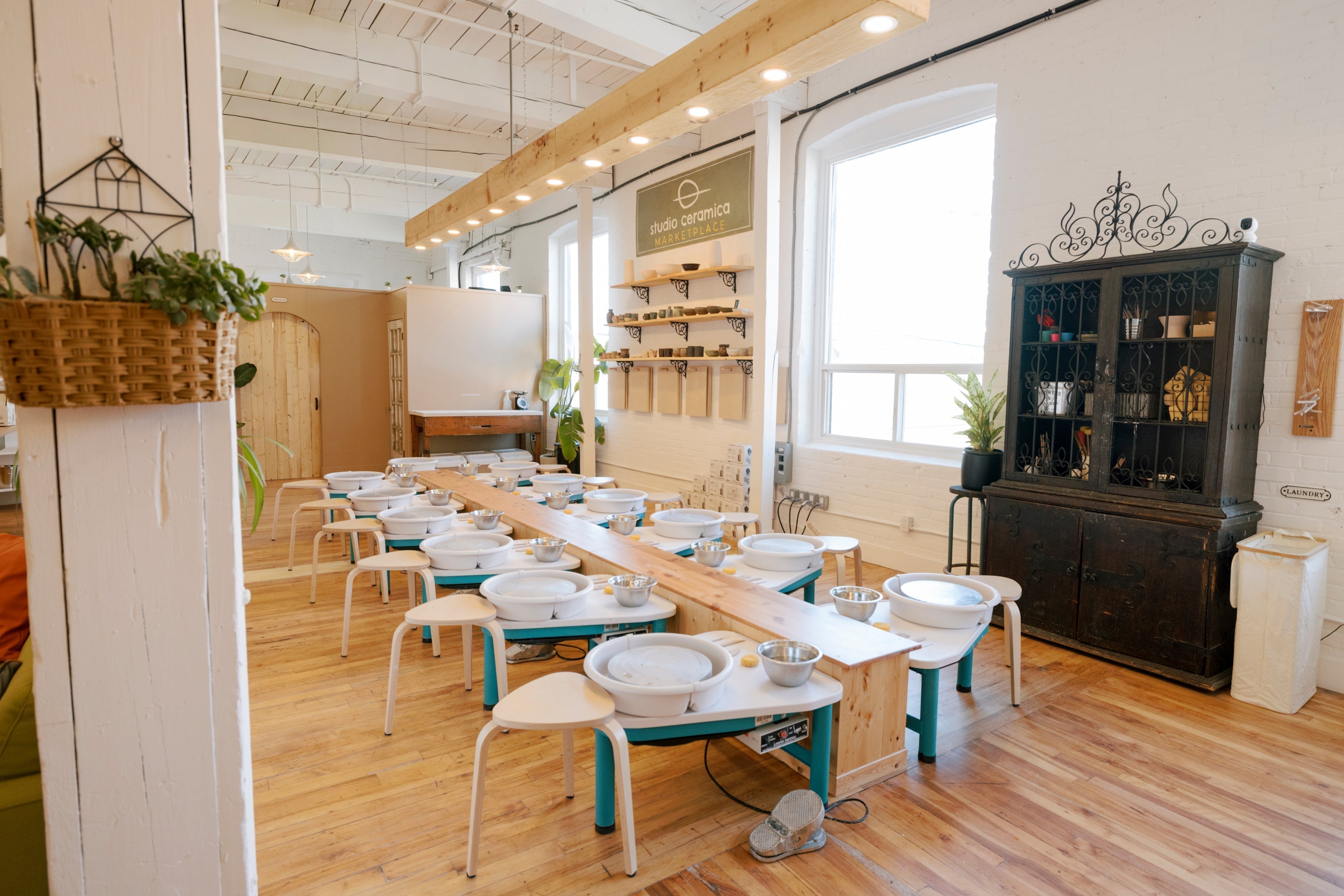 A pinterest worthy pottery studio with lots of wood, a center island flanked by pottery wheels and a wooden light beam. 