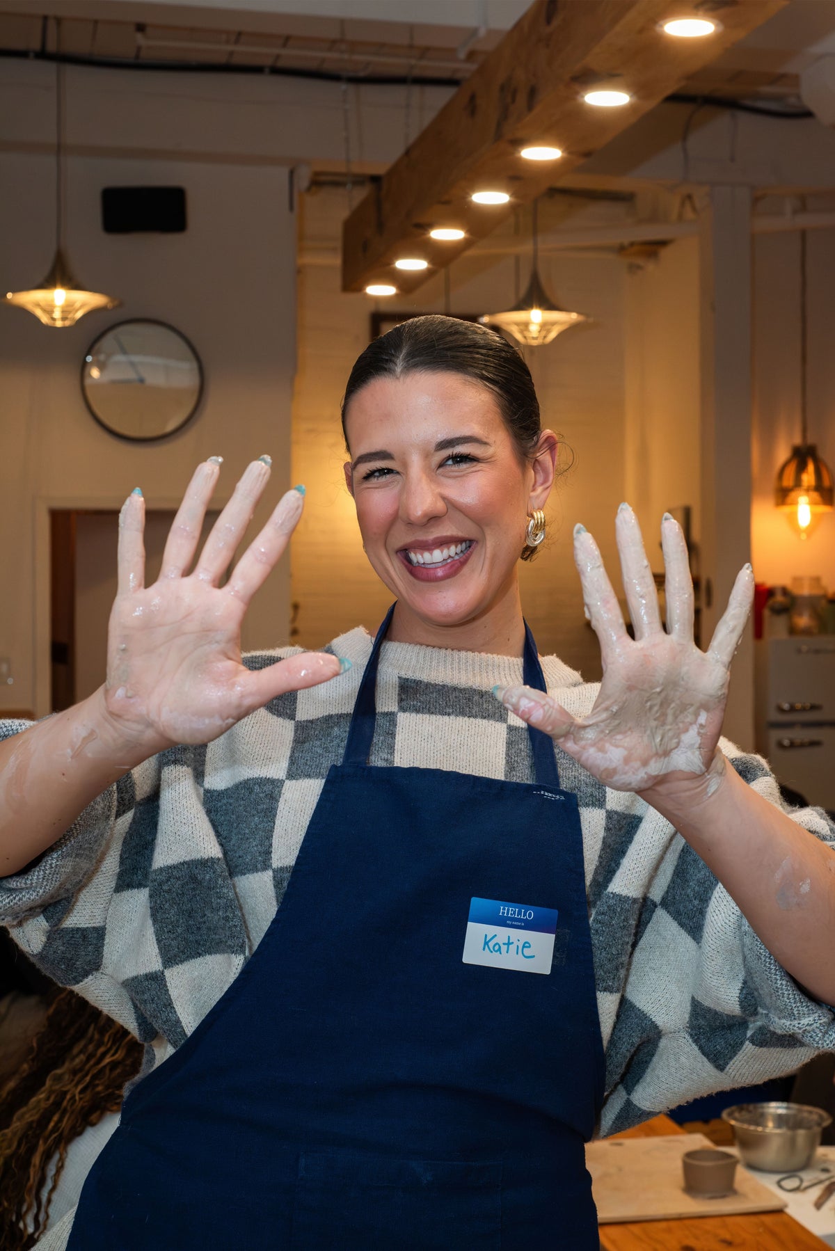 A smiling student in a studio apron holding up clay covered hands during a pottery date night class at Studio Ceramica in Toronto.