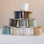Collection of stacked ceramic pots in various glaze colors on a white surface with a beige background