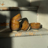 Four handmade ceramic cups on a wooden staircase in the sunlight